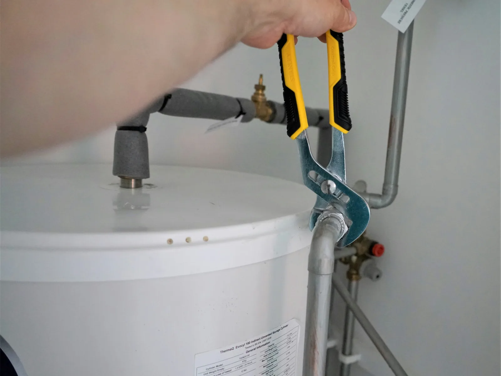 A plumber tightening pipe connections on a residential water heater tank with shutoff valve
